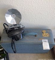 Vintage Konica Eye-Matic camera with large flash reflector and black strap sitting on top of the textured blue Monarch suitcase with brass clasps.