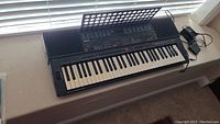 Full view of Yamaha electric keyboard placed on a window ledge showing built-in speakers on both ends and attached music sheet stand.