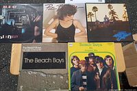 Five vinyl LP records from the 70s and early 80s including REO Speedwagon, Pat Benatar, Eagles, and The Beach Boys laid out on a table to show front covers.