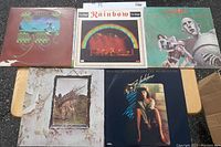 Five vinyl records displayed on a table, showing front covers of each album including Queen, Rainbow, and others, with visible wear on covers.