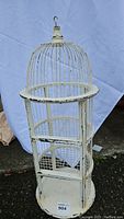 Full view of the vintage bird cage shelf, showing cream paint with wear and metal bars with wooden shelves inside