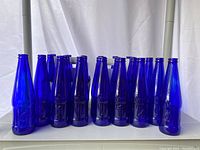 Row of cobalt blue glass bottles showing the front view with embossed design.