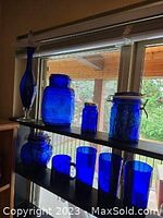 Photo of two clamp-top jars (one large and one small), decanter, flour canister, and a small blue glass container on a shelf by window.