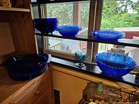 Wide shot of cobalt blue dinner plates, side plates, Pyrex clear bowls, iridescent creamer, and a large cobalt blue serving bowl on windowsill and shelf.