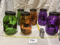 Six Halloween-themed glass jars in green, orange, and purple colors, each with black lids featuring star cutouts and Halloween silhouettes