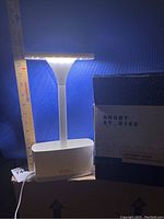 Front view of the white LED indoor planter illuminated and placed beside original box and ruler for size reference.