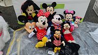 Lot of various Minnie and Mickey Mouse dolls and plush toys arranged on a surface, showing multiple styles and sizes.