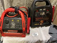 Two Motomaster power packs side by side on cloth backdrop. One is red with USB port and booster, the other is black Eliminator 700A.
