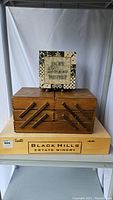 Photo of the three items: the wooden wine box on bottom, brown wooden segmented storage box in front, and decorative sewing box on top with inspirational quote on lid.