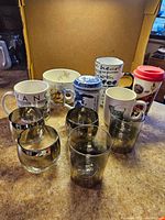 Full lot showing various coffee and tea mugs, Asian dragon tea cups, and mirrored tumblers arranged inside a box.