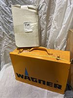 Closed yellow Wagner branded metal carrying case with handle and minor wear marks