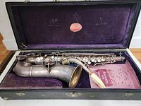 Alto saxophone body and neck laid in open black hard case with purple velvet lining