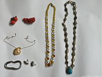 Overview of assorted vintage jewelry pieces including carved floral earrings, flower pendant necklace, bead necklaces, bracelet, and clip-on earrings on white background.