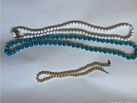 Three necklaces including white faux pearl bead necklaces and turquoise blue bead necklaces with metal clasps.