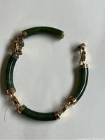 Full view of the jade bracelet showing five curved jade segments with gold connectors and a clasp with safety chain. One jade segment is detached.