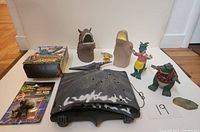 Dinosaur themed toys and collectibles arranged including wall decoration, figures, mask/puppet, and sealed card pack.