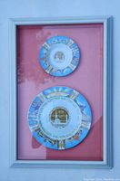Framed display with two decorative plates from 1939 San Francisco International Exposition. Shows overall lot with frame and plates. Visible clip loose on top.