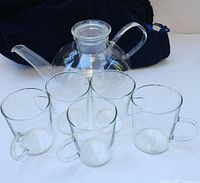 Front view of the tea pot and five glass cups arranged in front.