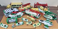 Photo showing a variety of 21 Hess toy vehicles including helicopters, trucks, fire engines, and cars arranged on cardboard surface.
