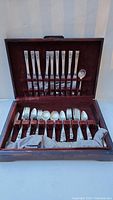 Fully opened box with utensils displayed in velvet-lined slots, showing varying sizes of forks and spoons with intricate handles.