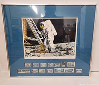Framed print showing astronaut descending lunar module ladder with space stamps below