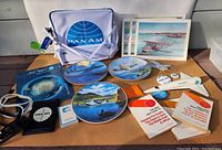 Wide shot of the collection showing flight bag, decorative plates, prints, model airplane, travel books, and small collectibles arranged on cardboard.