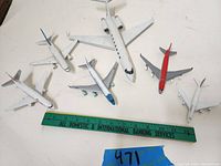 Six die-cast model airplanes laid out on a table with a green ruler for scale, showing different airline liveries and sizes around 5-7 inches long.