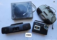 Top view of four vintage audio devices: dust cover turntable, Sony cassette player boombox, another boombox, and a Sanyo AM/FM radio cassette player.