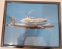 Framed photo of NASA Space Shuttle on 747 with visible reflection and simple metal frame.