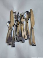 Top-down photo of the silverware set showing hammered texture and rivet detail on handles including knives, forks, teaspoons, and tablespoons.