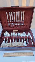 Full open storage box showing the entire silverware set including knives, forks, spoons, and serving pieces arranged in velvet-lined slots.