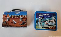 Photo of the front and top side of two vintage lunch boxes. Left is Tom Corbett Space Cadet themed with space scene and rocket illustrations. Right is G Whiz 6" blue lunch box with three space cadets and moon scene.