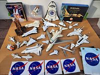 Top view of all items including space shuttle models, NASA patches, books, and a large space shuttle attached to carrier aircraft model.