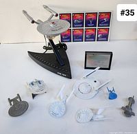 Image showing various Star Trek ship models including USS Enterprise models, a Star Trek phone, small ship figures, and hologram cards in the background.