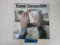 Front of the Comic Connection game box showing title, Superman logo, hands arranging comic panels.