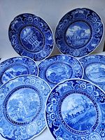 Photo shows seven blue and white decorative plates arranged together, depicting Columbia University scenes, floral borders, and Latin inscriptions.