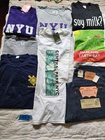 Top view showing eight vintage t-shirts with various logos, including NYU, soy milk?, Oakland Earth Day, and Central Park NYC, plus the Levi's jeans folded showing multiple original tags.