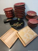 Set of stacked red lacquer bowls, stacked red lacquer plates, stacked black plates with floral design, and two wooden boxes