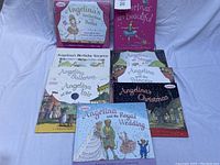 Photo of nine Angelina Ballerina children's books laid out on a white surface, showing colorful illustrated covers with titles.