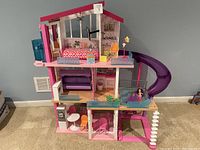 Front view of Barbie Dream House showing three levels with furniture, pink exterior, purple slide and some small accessories.
