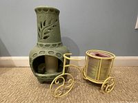 The clay chimenea candleholder and the metal tricycle candleholder side by side on carpet, wall background
