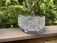 Side view of the clear three-legged crystal bowl placed outdoors showing intricate cut glass patterns and round legs.