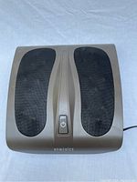 Top view photo of Homedics foot massager showing black mesh footrests and central power button.