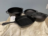 Set of four cast iron cookware pieces displayed including a grill pan, two Dutch ovens with lids, and a skillet.