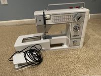 Side view of white Necchi 575 FA sewing machine with foot pedal on beige carpet background