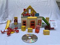 Full view of doll house with accessories arranged around it, including two child figures, slide, swivel seesaw, TV, and various furniture pieces. CD shown for size reference but not included.