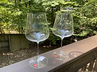 Two clear Spiegelau wine glasses or water goblets on a wooden railing in natural light.