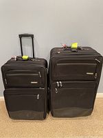 Front view of two black rolling suitcases with front zippered compartments and visible wear