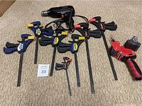 Nine clamps of various sizes and brands including Irwin Quick-Grip and Craftsman bar clamps and a handheld tape dispenser on carpeted floor.