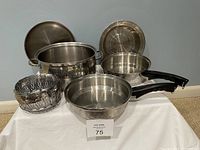 Five stainless steel cookware items including a Dutch oven with lid, steamer basket, and two handled pans including double boiler insert pan arranged on white surface.